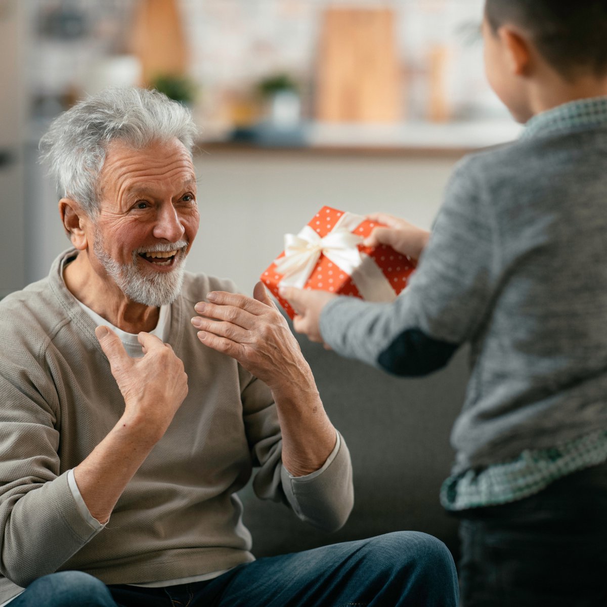 Oude man met grijze haren en baard, die glimlachend een rood cadeau met witte stippen ontvangt van een jongen.