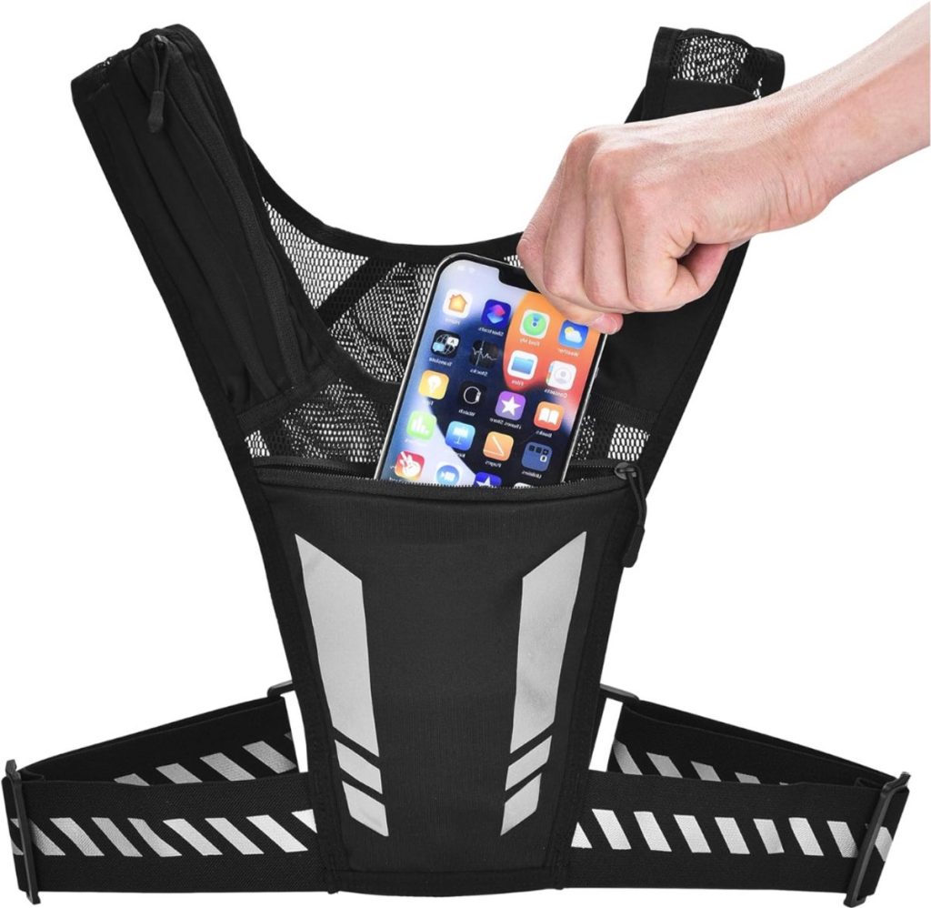 Een hand plaatst een smartphone in het voorvak van een zwart, reflecterend loopvest.