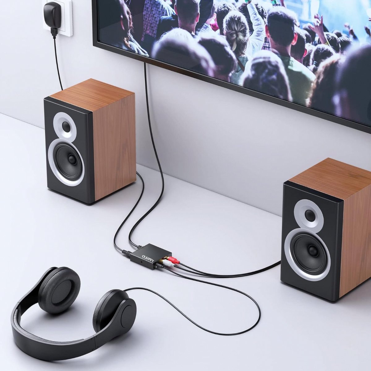 Zwarte Clerby audioconverter aangesloten tussen een TV, twee houten speakers en een koptelefoon.