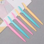 Zes gezichts-scheermesjes in pastelkleuren roze, turquoise en geel, op papier.