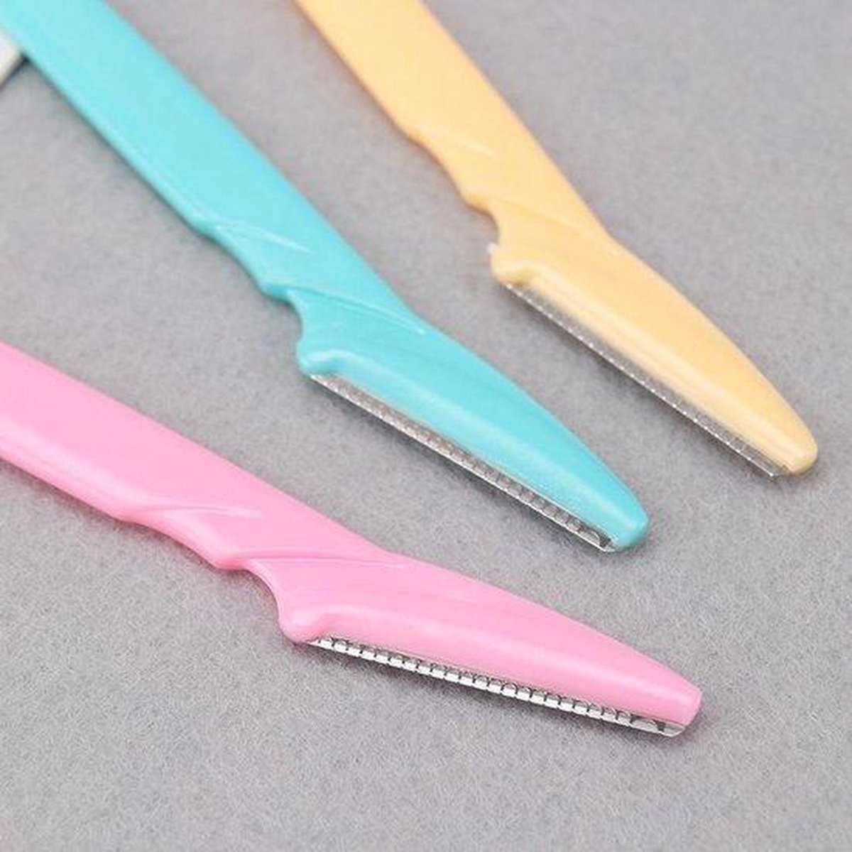 Close-up van roze, turquoise en gele gezichts-scheermesjes met metalen bladen.